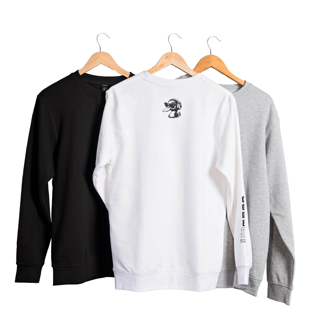 Three sweatshirts in black, white, and gray hanging on wooden hangers against a white background.